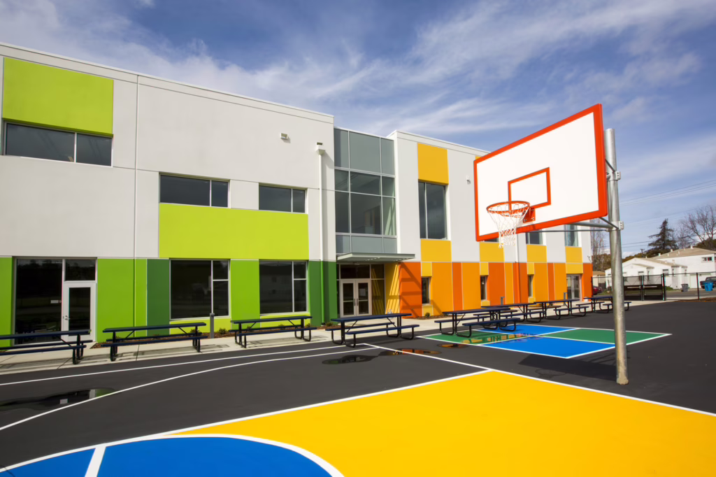 Modern charter school building with bright green, yellow, and orange panels beside a colorful outdoor basketball court, showcasing Blueprint’s expertise in designing engaging, student-centered school facilities.